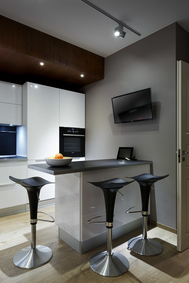 This is an example of a contemporary kitchen in Saint Petersburg with flat-panel cabinets, white cabinets, black appliances, light hardwood floors and a peninsula.