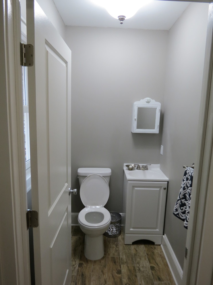 Design ideas for a small transitional powder room in New York with an integrated sink, recessed-panel cabinets, white cabinets, solid surface benchtops, a two-piece toilet, grey walls and ceramic floors.