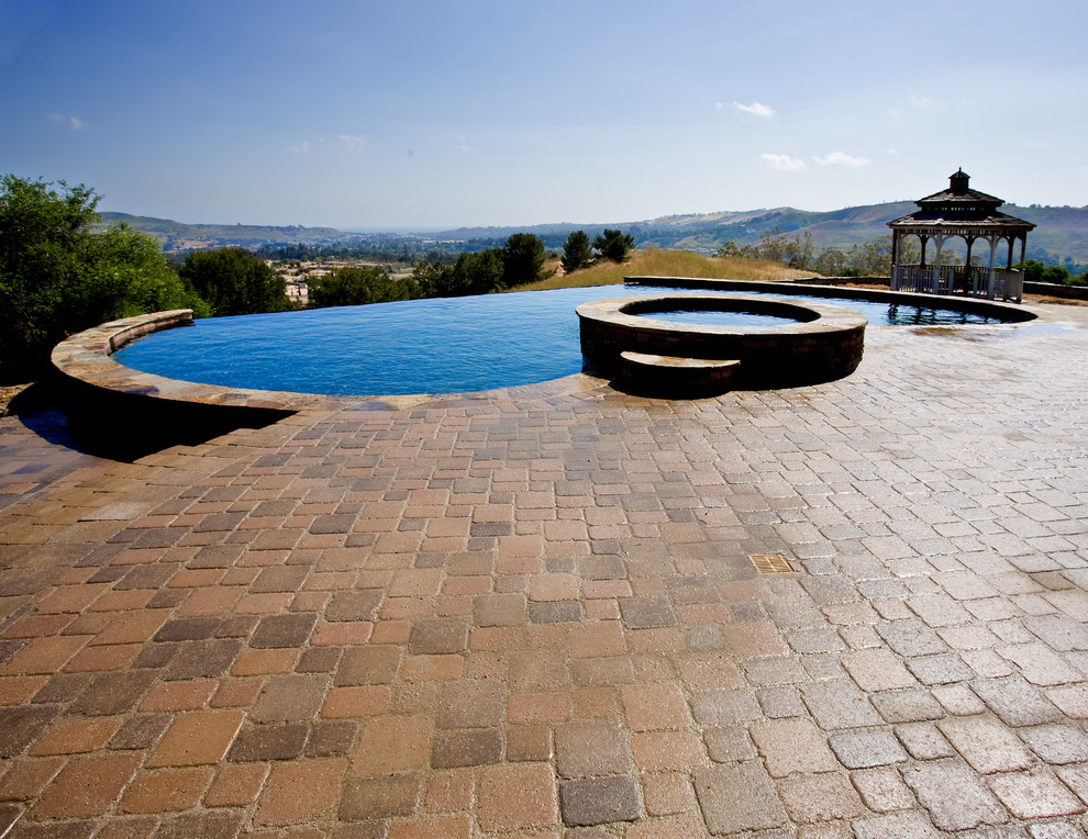 Inspiration for a backyard concrete paver and custom-shaped infinity pool house remodel in Orange County