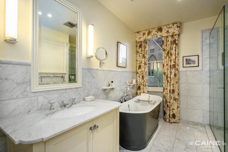 Photo of a traditional bathroom in Melbourne with an undermount sink, furniture-like cabinets, beige cabinets, marble benchtops, a freestanding tub, a corner shower, gray tile, stone tile, beige walls and marble floors.