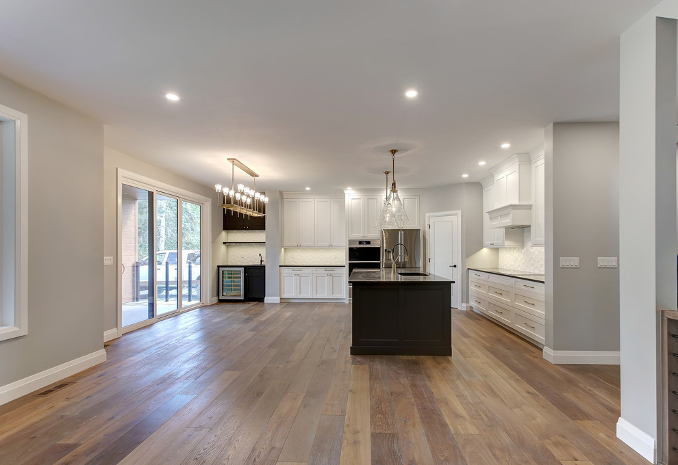 Open concept kitchen - mid-sized transitional l-shaped medium tone wood floor and brown floor open concept kitchen idea in Edmonton with an undermount sink, recessed-panel cabinets, white cabinets, quartz countertops, white backsplash, ceramic backsplash, stainless steel appliances, an island and black countertops