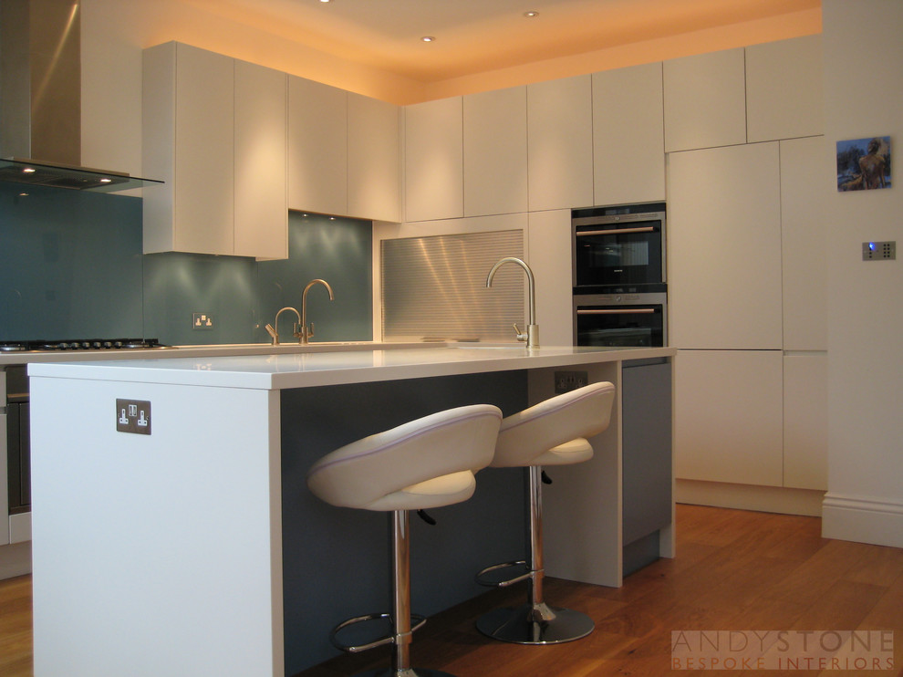 Photo of a contemporary eat-in kitchen in London with an undermount sink, flat-panel cabinets, white cabinets, blue splashback, glass sheet splashback and stainless steel appliances.