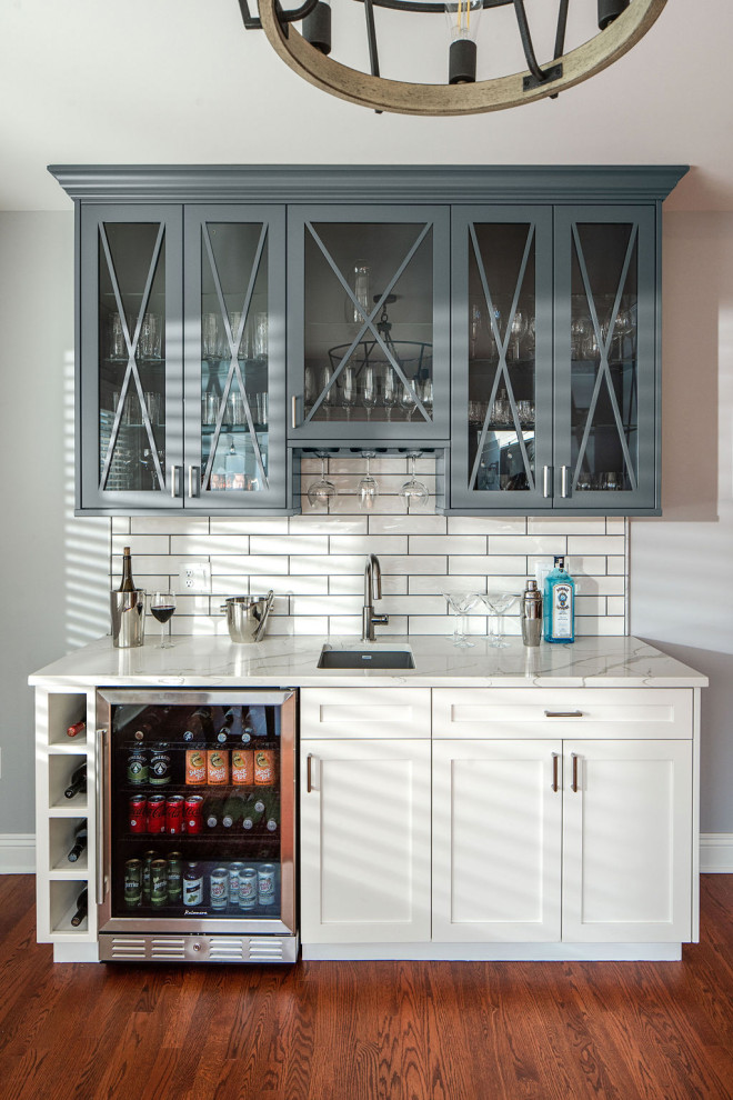 Inspiration for a mid-sized transitional single-wall wet bar in Columbus with an undermount sink, shaker cabinets, white splashback, subway tile splashback, medium hardwood floors, brown floor and white benchtop.