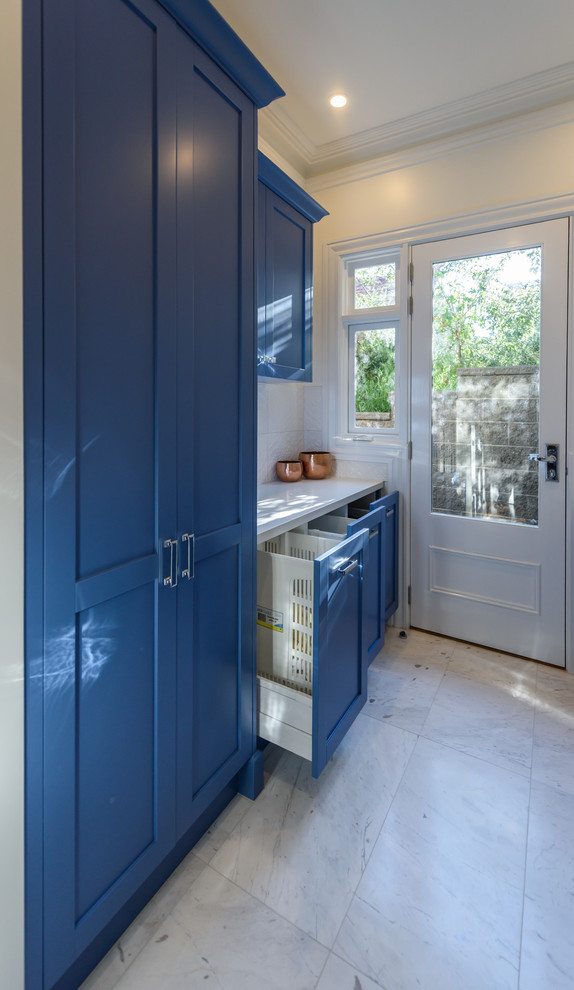 This is an example of a mid-sized traditional galley dedicated laundry room in Melbourne with recessed-panel cabinets, blue cabinets, quartz benchtops, white walls, marble floors and a side-by-side washer and dryer.