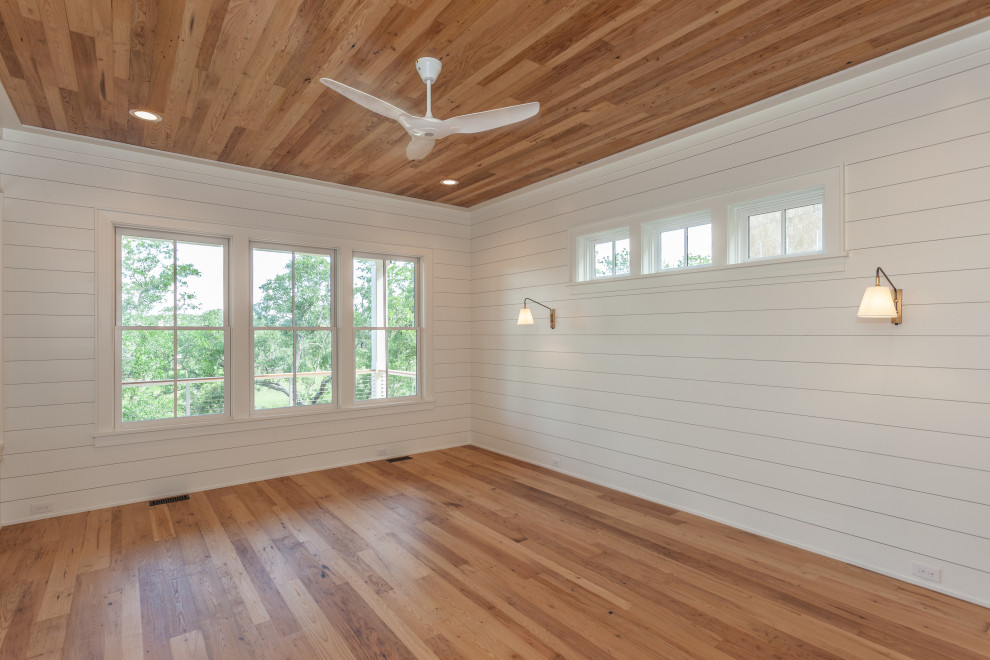 Photo of a large beach style master bedroom in Charleston with white walls, light hardwood floors, wood and planked wall panelling.