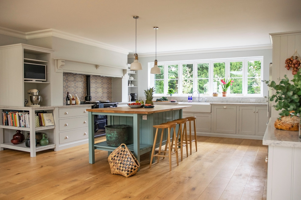 This is an example of a large transitional u-shaped eat-in kitchen in Hertfordshire with a double-bowl sink, shaker cabinets, white cabinets, quartz benchtops, grey splashback, stone slab splashback, stainless steel appliances, medium hardwood floors, with island, brown floor and grey benchtop.