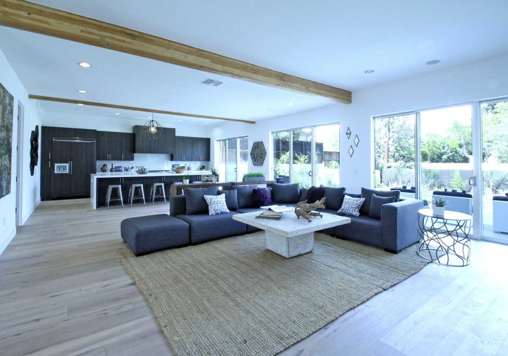 This is an example of a large transitional open concept family room in Los Angeles with white walls, light hardwood floors, brown floor, a standard fireplace, a plaster fireplace surround and a wall-mounted tv.