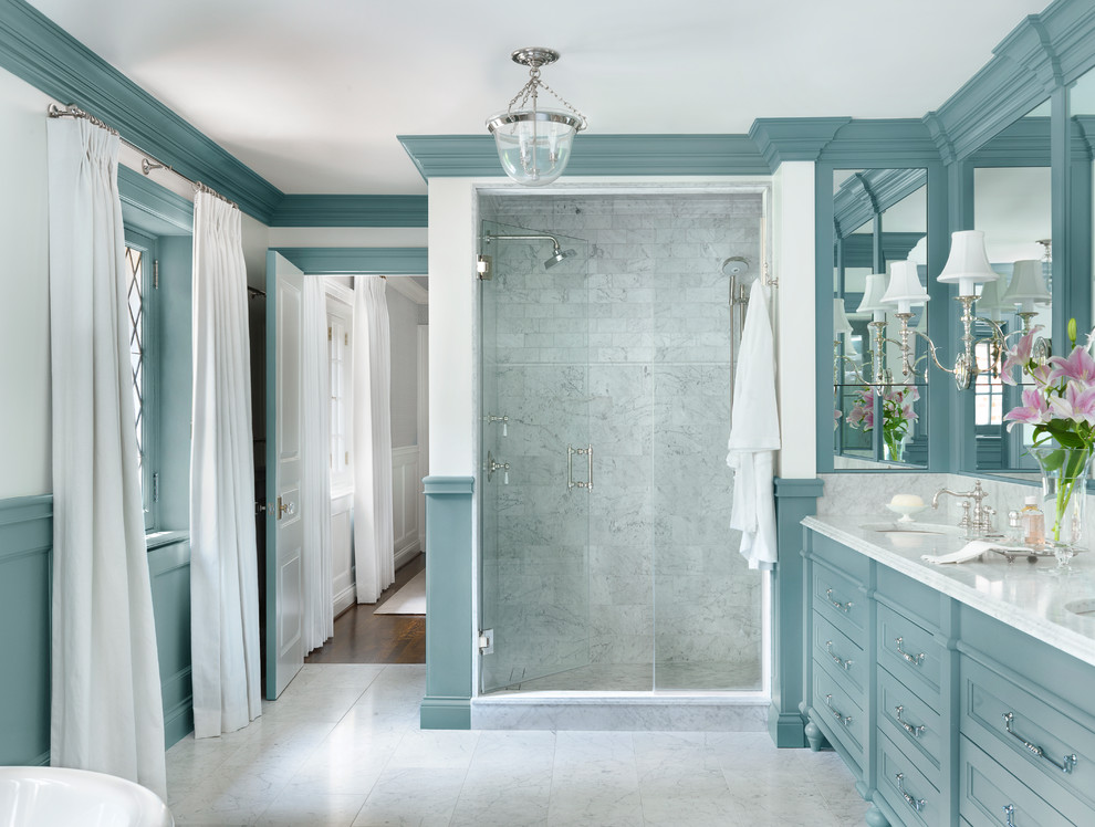 This is an example of a mid-sized traditional master bathroom in St Louis with blue cabinets, an alcove shower, marble floors, an undermount sink, marble benchtops, white floor, a hinged shower door, recessed-panel cabinets, gray tile and white walls.