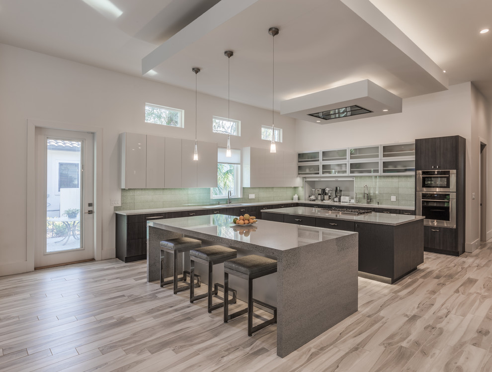 Contemporary l-shaped kitchen in Jacksonville with an undermount sink, flat-panel cabinets, white cabinets, green splashback, glass tile splashback, stainless steel appliances, multiple islands and beige floor.