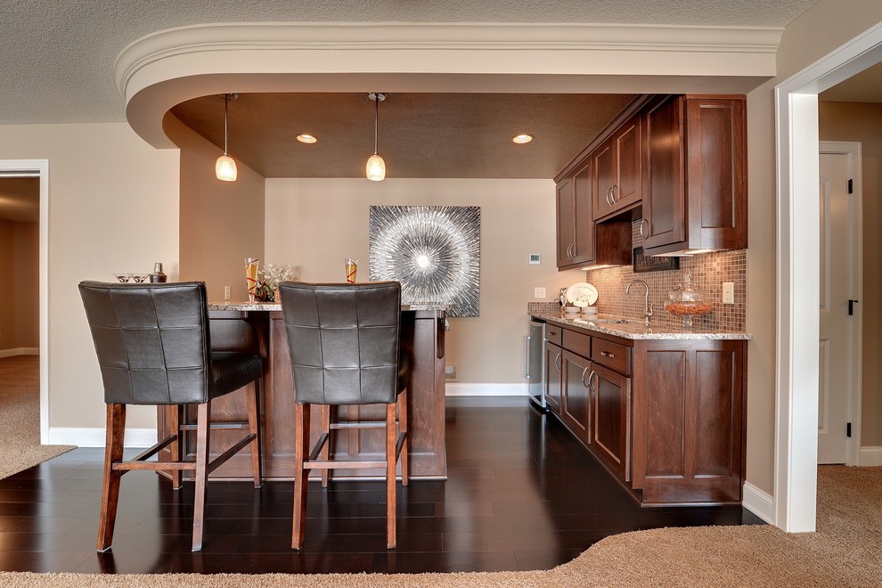 This is an example of a traditional u-shaped seated home bar in Minneapolis with dark hardwood floors, shaker cabinets, dark wood cabinets, beige splashback, mosaic tile splashback and brown floor.