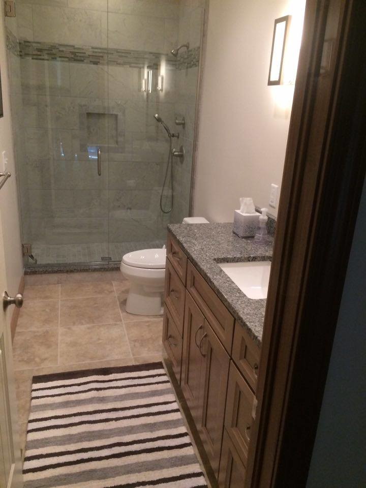 This is an example of a mid-sized transitional master bathroom in Other with recessed-panel cabinets, medium wood cabinets, an alcove shower, a one-piece toilet, gray tile, porcelain tile, grey walls, porcelain floors, an undermount sink and granite benchtops.