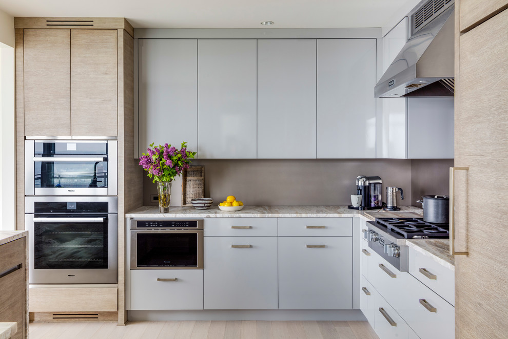 This is an example of a large contemporary l-shaped kitchen in Boston with flat-panel cabinets, grey cabinets, marble benchtops, grey splashback, stainless steel appliances, beige floor, light hardwood floors and multi-coloured benchtop.