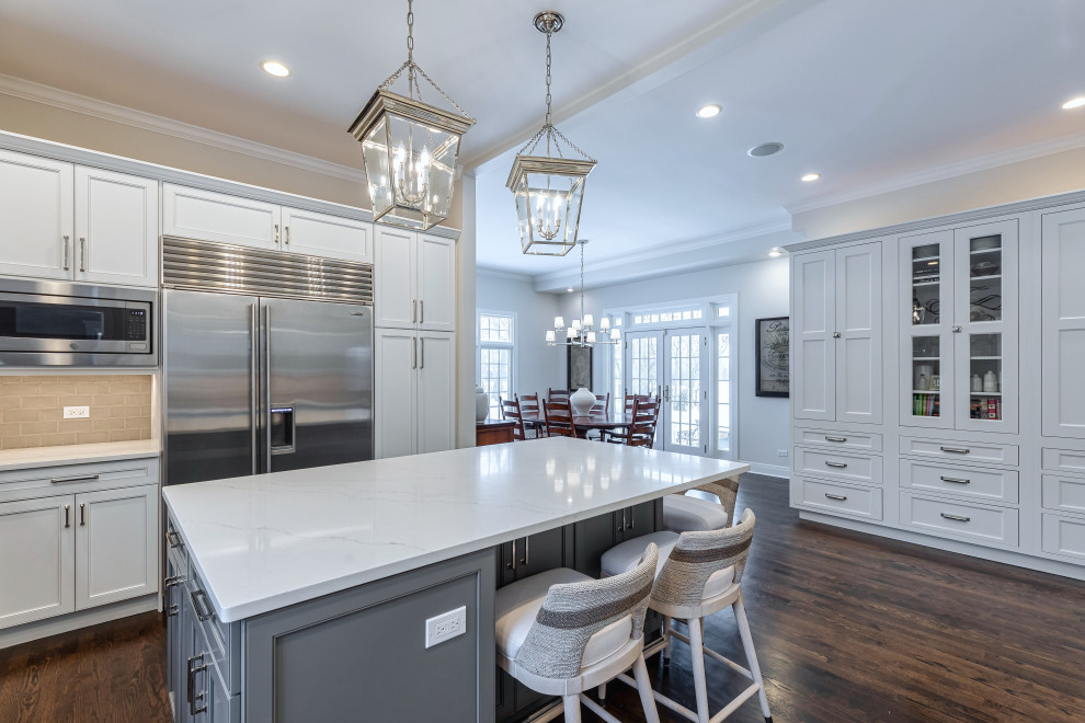 Inspiration for a large transitional u-shaped dark wood floor and brown floor eat-in kitchen remodel in Chicago with a farmhouse sink, beaded inset cabinets, white cabinets, quartz countertops, gray backsplash, glass tile backsplash, stainless steel appliances, an island and white countertops