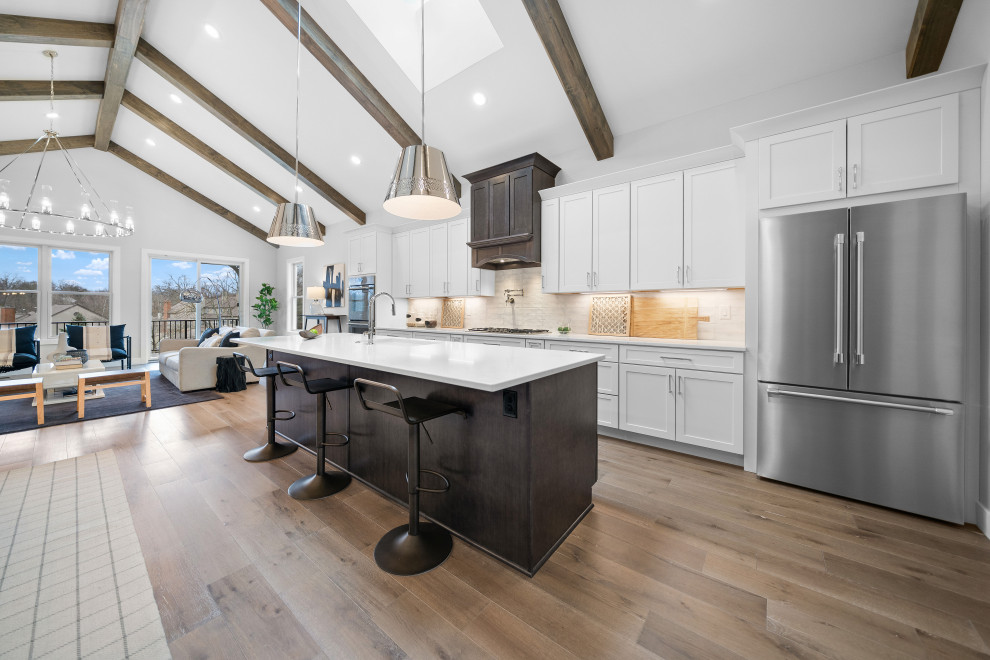 Inspiration for a transitional galley medium tone wood floor and vaulted ceiling open concept kitchen remodel in Cincinnati with an undermount sink, shaker cabinets, white cabinets, quartz countertops, white backsplash, ceramic backsplash, stainless steel appliances, an island and white countertops