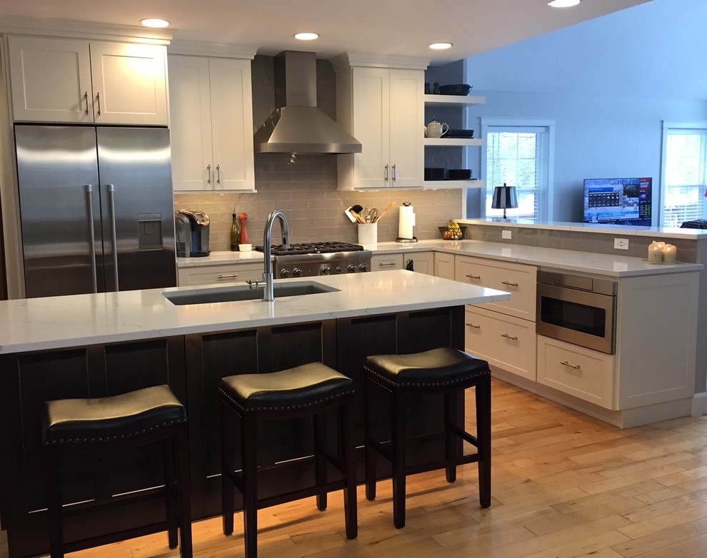 Open concept kitchen - transitional l-shaped light wood floor open concept kitchen idea with recessed-panel cabinets, an island, an undermount sink, white cabinets, quartz countertops, gray backsplash, stainless steel appliances and ceramic backsplash
