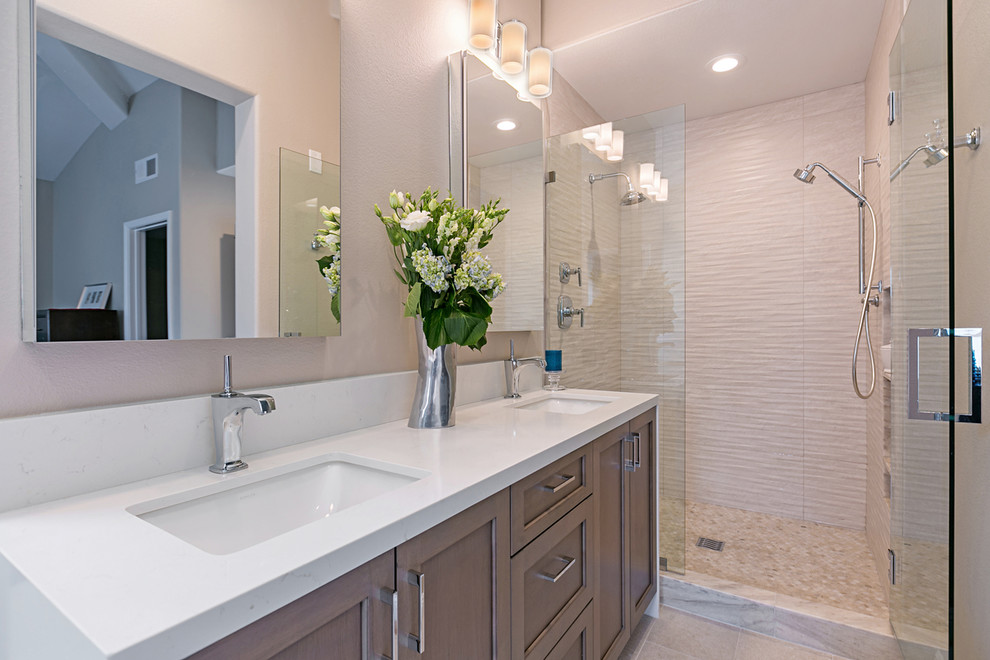 This is an example of a mid-sized transitional master bathroom in San Diego with shaker cabinets, brown cabinets, a freestanding tub, a double shower, a one-piece toilet, beige tile, porcelain tile, grey walls, porcelain floors, an undermount sink, engineered quartz benchtops, grey floor and a hinged shower door.
