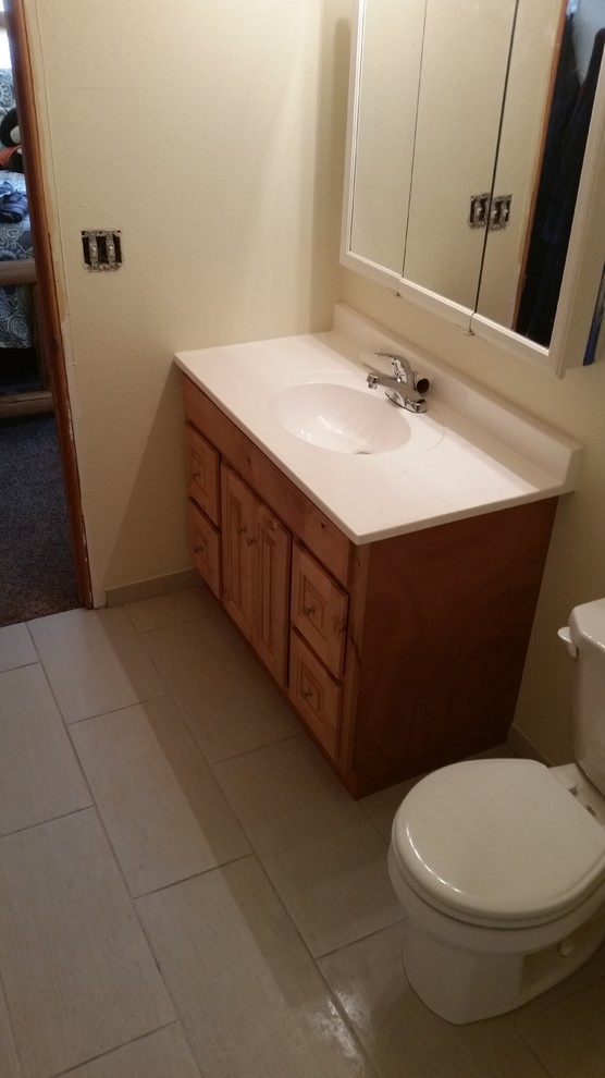 Photo of a mid-sized transitional 3/4 bathroom in Seattle with raised-panel cabinets, light wood cabinets, an alcove tub, a shower/bathtub combo, a two-piece toilet, beige tile, ceramic tile, beige walls, laminate floors, an integrated sink, limestone benchtops, beige floor and a shower curtain.