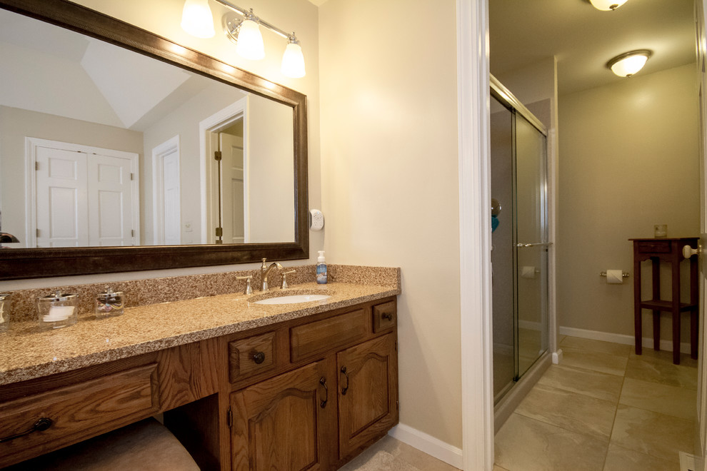 Design ideas for a mid-sized traditional master bathroom in St Louis with raised-panel cabinets, medium wood cabinets, a drop-in tub, an alcove shower, beige tile, ceramic tile, beige walls, ceramic floors, an undermount sink, laminate benchtops, beige floor and a sliding shower screen.