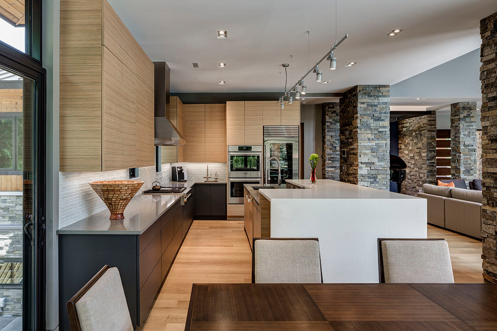 This is an example of a contemporary l-shaped kitchen in Detroit with an undermount sink, flat-panel cabinets, light wood cabinets, grey splashback, stainless steel appliances, light hardwood floors, with island and grey benchtop.