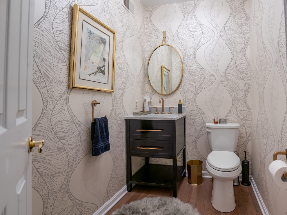 Inspiration for a small traditional cloakroom in Baltimore with freestanding cabinets, black cabinets, a two-piece toilet, beige walls, medium hardwood flooring, a submerged sink, marble worktops, brown floors, grey worktops, a freestanding vanity unit and wallpapered walls.