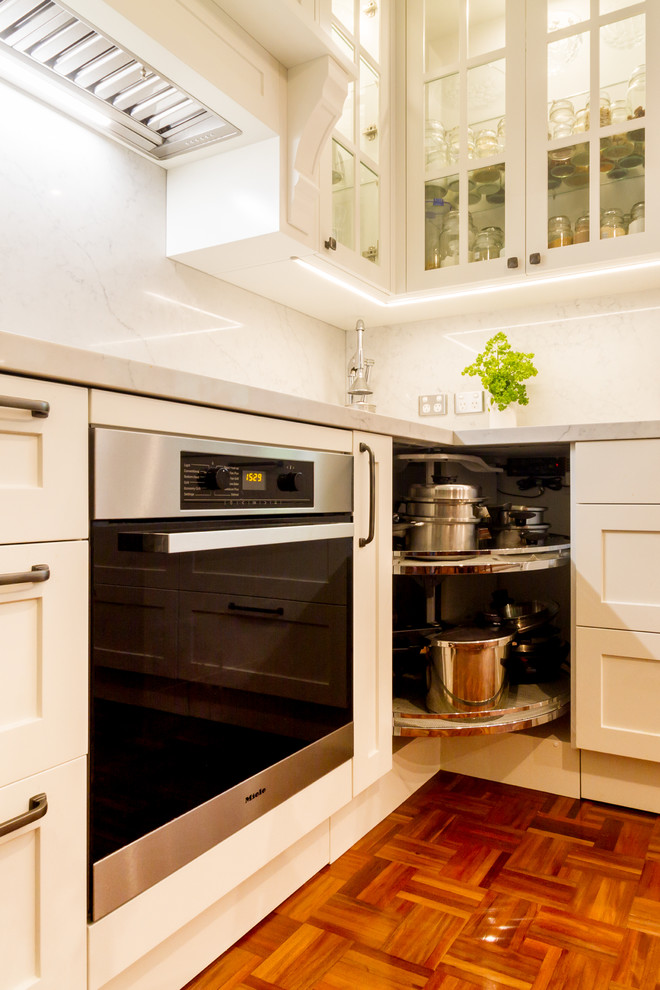 Photo of a mid-sized traditional u-shaped eat-in kitchen in Melbourne with a drop-in sink, shaker cabinets, white cabinets, marble benchtops, white splashback, marble splashback, stainless steel appliances, medium hardwood floors, a peninsula, brown floor and white benchtop.