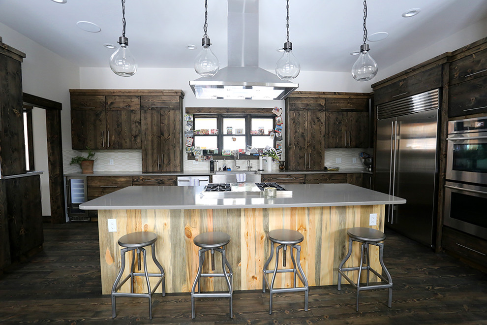 Example of a large transitional u-shaped brown floor and dark wood floor kitchen design with a farmhouse sink, stainless steel appliances, flat-panel cabinets, dark wood cabinets, solid surface countertops, white backsplash, ceramic backsplash and an island