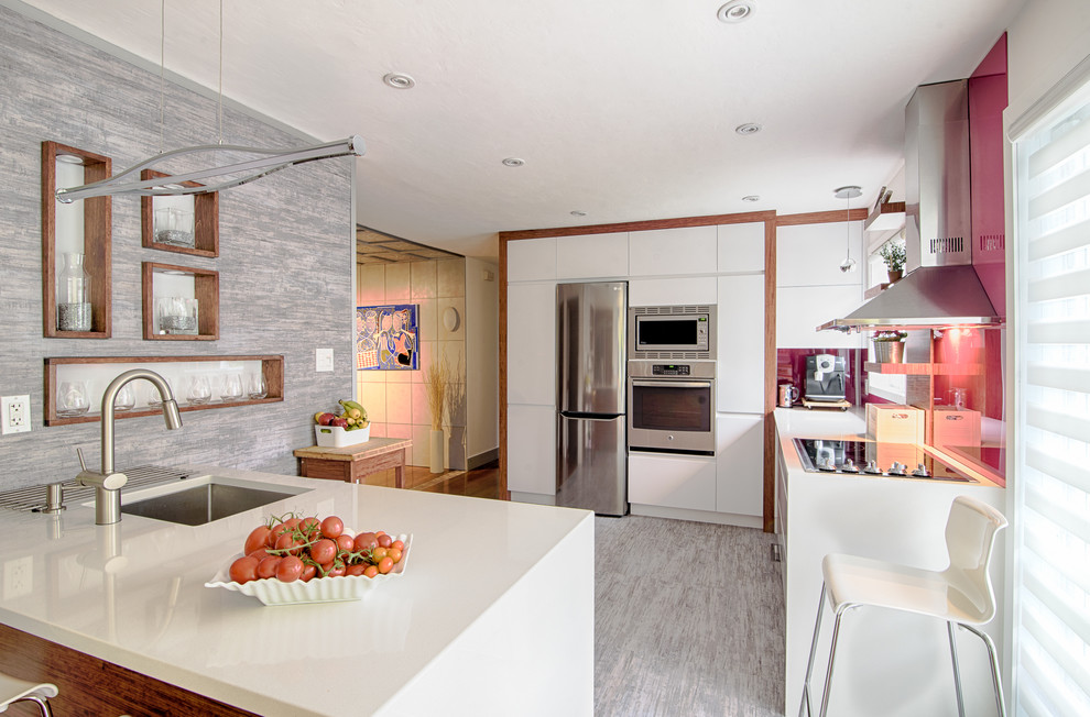 Inspiration for a large contemporary galley eat-in kitchen in Montreal with an undermount sink, flat-panel cabinets, white cabinets, quartz benchtops, pink splashback, stainless steel appliances, a peninsula, grey floor and glass sheet splashback.