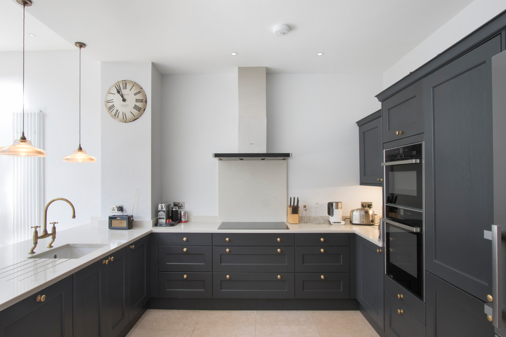 This is an example of a mid-sized transitional u-shaped kitchen in Other with limestone floors, beige floor, beige benchtop, an undermount sink, shaker cabinets, black cabinets, beige splashback, black appliances, a peninsula and granite benchtops.