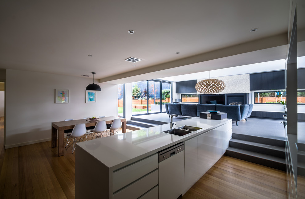 This is an example of a large modern l-shaped eat-in kitchen in Melbourne with a drop-in sink, flat-panel cabinets, dark wood cabinets, quartz benchtops, metallic splashback, mirror splashback, stainless steel appliances, medium hardwood floors and with island.
