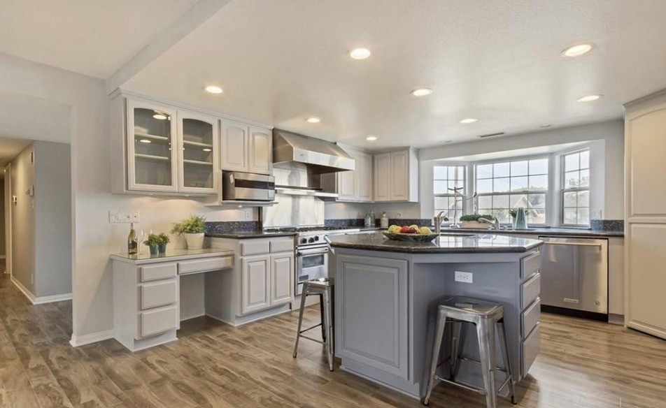 This is an example of a mid-sized transitional u-shaped eat-in kitchen in Orange County with an undermount sink, raised-panel cabinets, grey cabinets, granite benchtops, black splashback, marble splashback, stainless steel appliances, laminate floors, with island, grey floor and black benchtop.