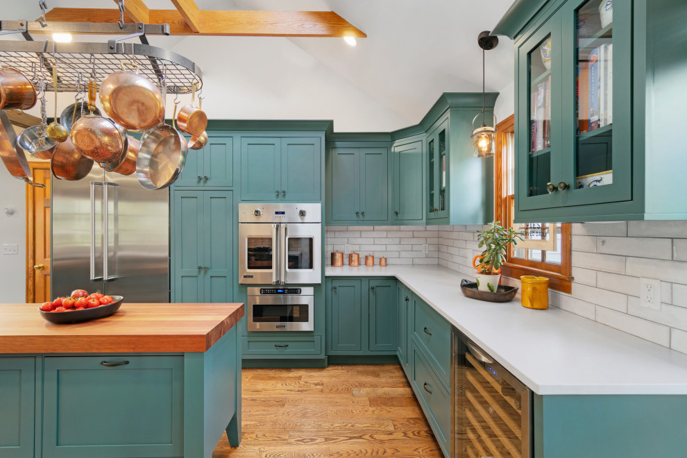 Inspiration for a large transitional l-shaped medium tone wood floor, brown floor and exposed beam enclosed kitchen remodel in Providence with a farmhouse sink, shaker cabinets, green cabinets, quartzite countertops, white backsplash, ceramic backsplash, stainless steel appliances, two islands and white countertops