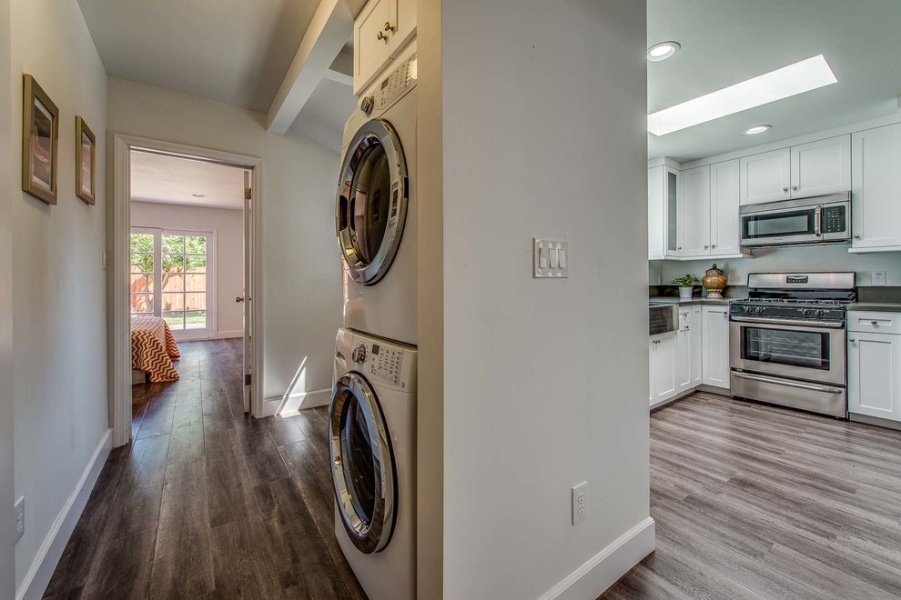 Inspiration for a laundry cupboard in Los Angeles with a single-bowl sink, shaker cabinets, white cabinets, white walls, medium hardwood floors and a stacked washer and dryer.
