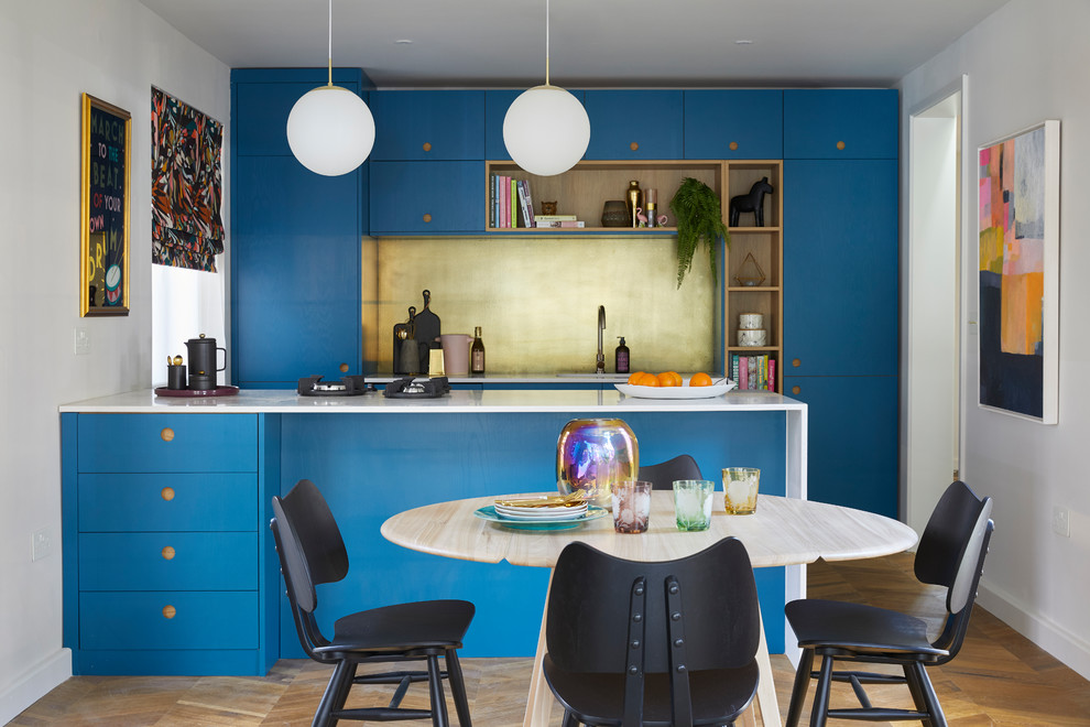 Photo of a mid-sized contemporary single-wall eat-in kitchen in London with an undermount sink, flat-panel cabinets, blue cabinets, solid surface benchtops, metallic splashback, metal splashback, black appliances, medium hardwood floors, brown floor, white benchtop and a peninsula.