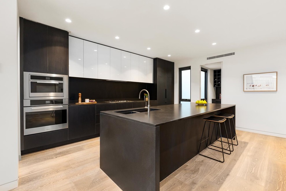 Photo of a large contemporary u-shaped open plan kitchen in Melbourne with an integrated sink, flat-panel cabinets, black cabinets, marble benchtops, black splashback, marble splashback, black appliances, ceramic floors, with island, brown floor and black benchtop.