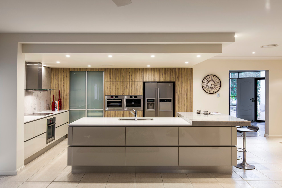 Mid-sized modern l-shaped kitchen pantry in Brisbane with a double-bowl sink, flat-panel cabinets, beige cabinets, quartz benchtops, white splashback, marble splashback, stainless steel appliances, porcelain floors, with island and beige floor.