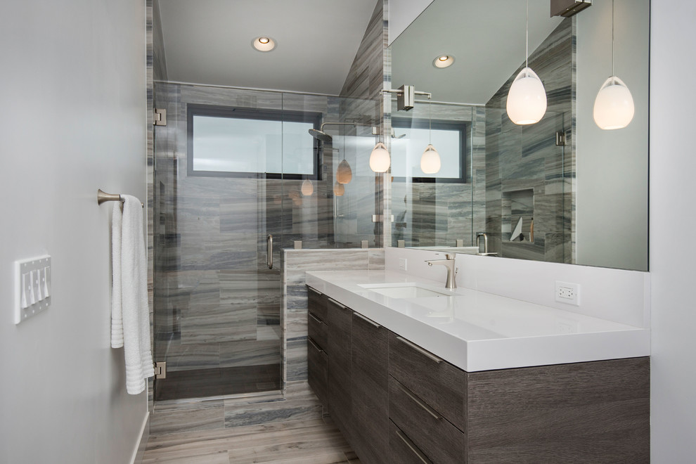 Photo of a large beach style 3/4 bathroom in Tampa with flat-panel cabinets, light wood cabinets, porcelain floors, grey floor, an alcove shower, a one-piece toilet, gray tile, cement tile, white walls, an undermount sink, engineered quartz benchtops and a hinged shower door.