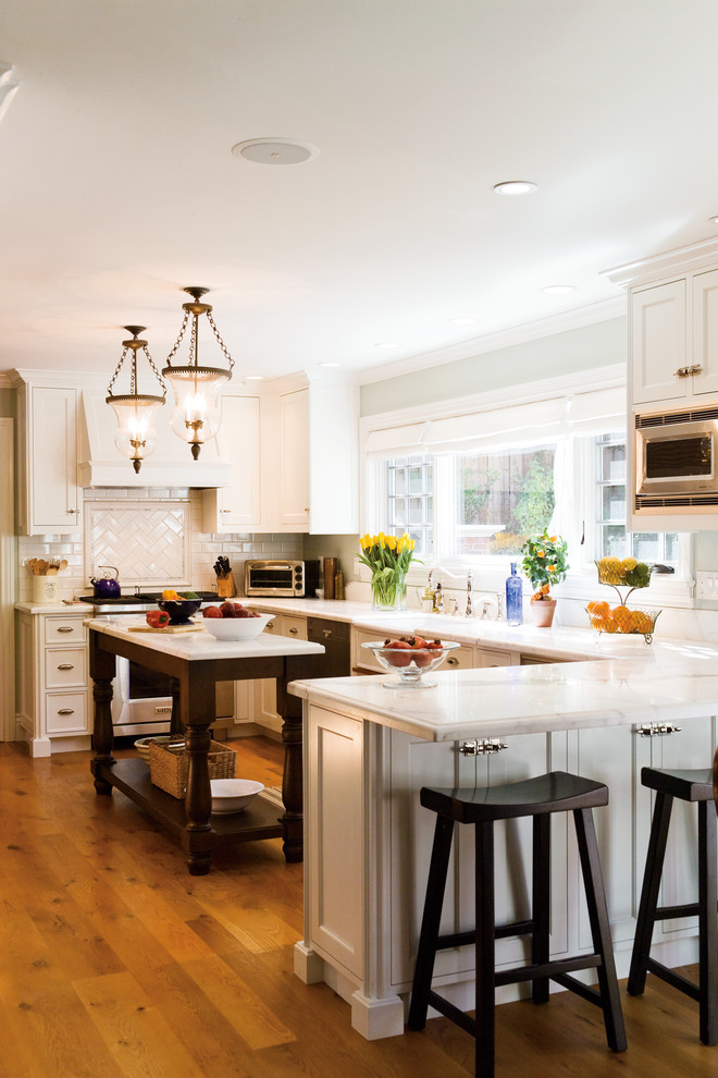 Mid-sized traditional u-shaped eat-in kitchen in San Francisco with ceramic splashback, white cabinets, white splashback, stainless steel appliances, marble benchtops, medium hardwood floors, with island, a farmhouse sink and shaker cabinets.