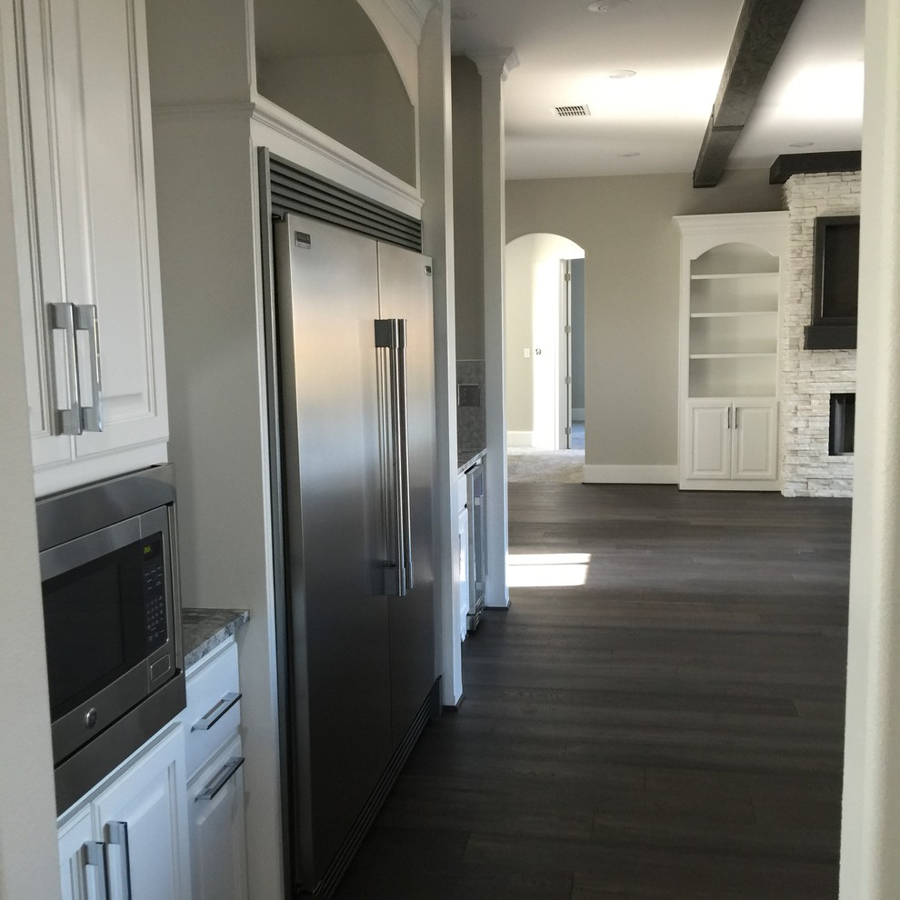 Open concept kitchen - mid-sized transitional l-shaped dark wood floor and brown floor open concept kitchen idea in Orange County with a farmhouse sink, raised-panel cabinets, white cabinets, marble countertops, metallic backsplash, metal backsplash, stainless steel appliances and an island
