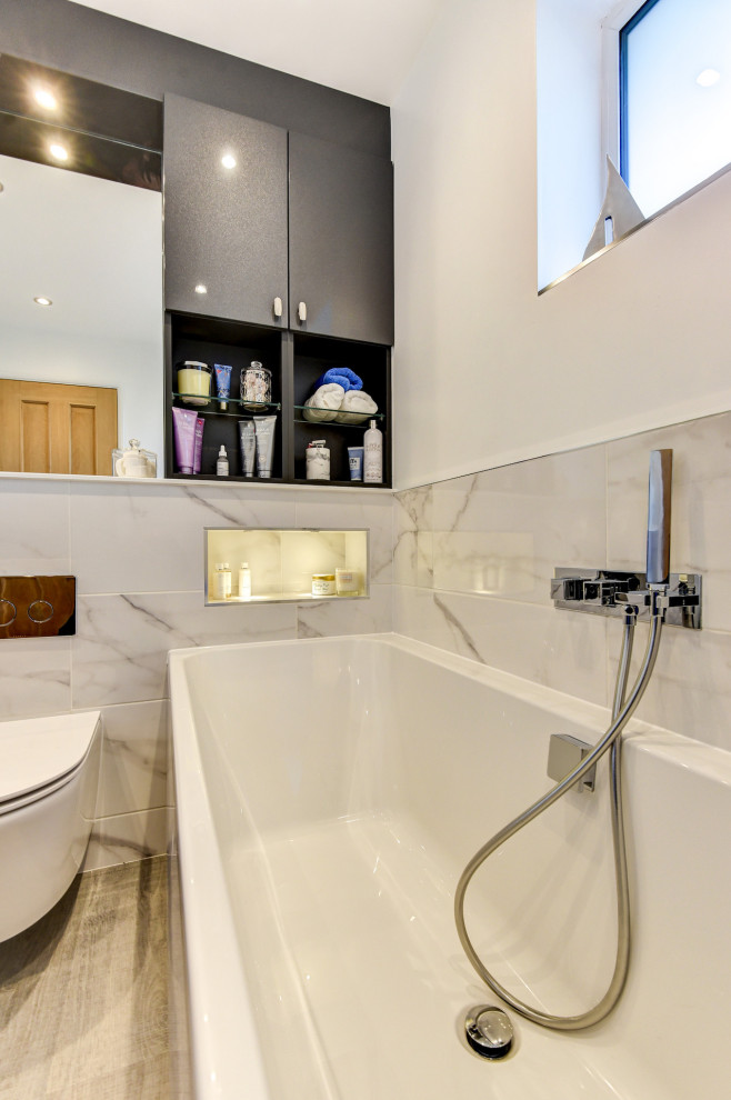 Photo of a small modern kids bathroom in Sussex with flat-panel cabinets, grey cabinets, a drop-in tub, a shower/bathtub combo, a wall-mount toilet, white tile, marble, white walls, laminate floors, an integrated sink, marble benchtops, brown floor, a shower curtain, a niche, a single vanity and a built-in vanity.