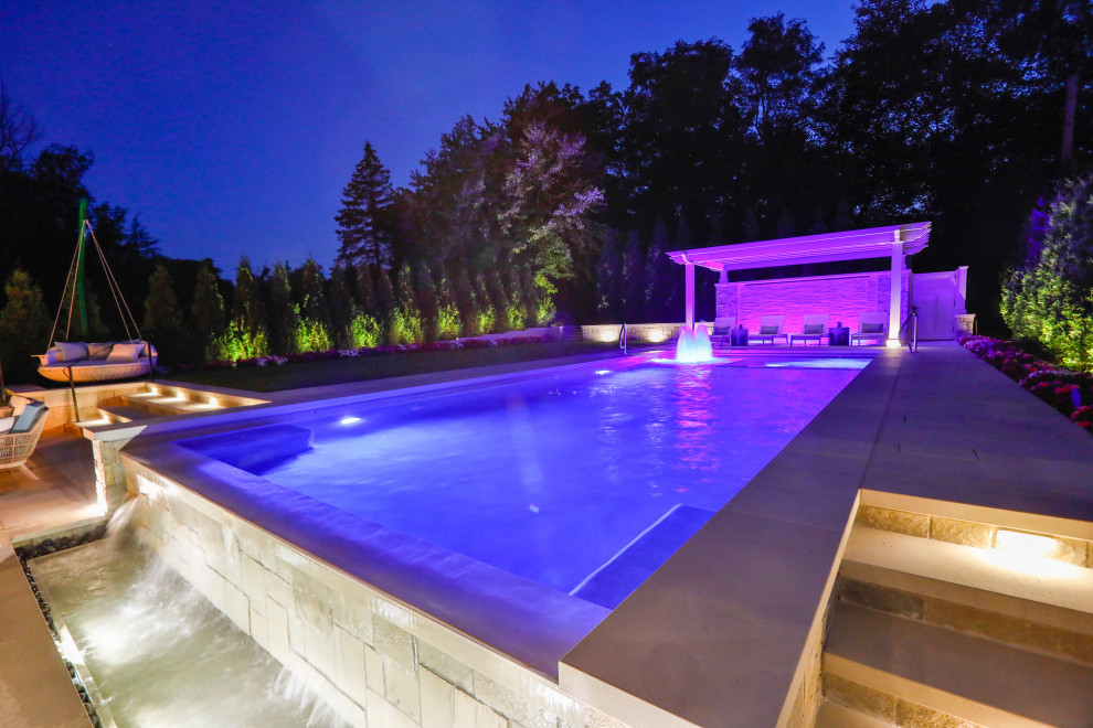 Modelo de piscina alargada tradicional de tamaño medio rectangular en patio trasero con paisajismo de piscina y adoquines de piedra natural