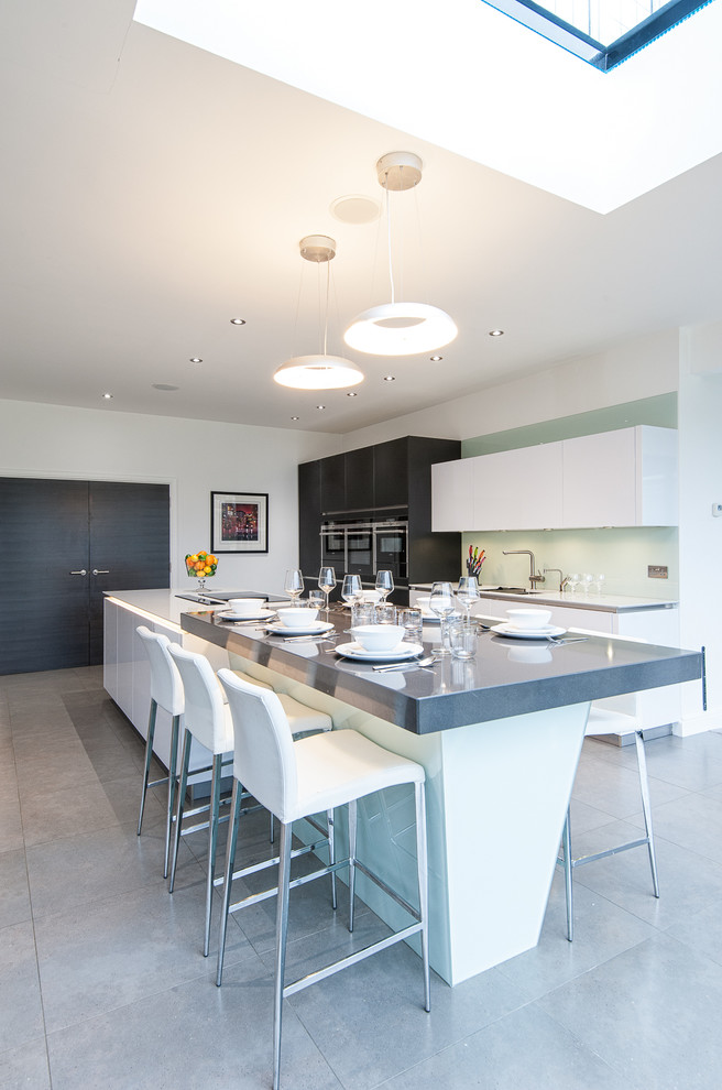 Inspiration for a large contemporary single-wall eat-in kitchen in London with flat-panel cabinets, grey cabinets, stainless steel appliances, with island, an undermount sink, white splashback, glass sheet splashback and porcelain floors.