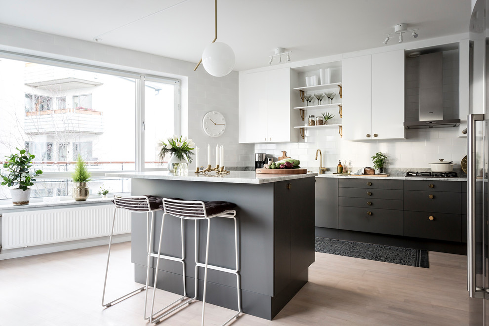 This is an example of a mid-sized scandinavian galley kitchen in Stockholm with flat-panel cabinets, marble benchtops, light hardwood floors, with island, black cabinets and white splashback.