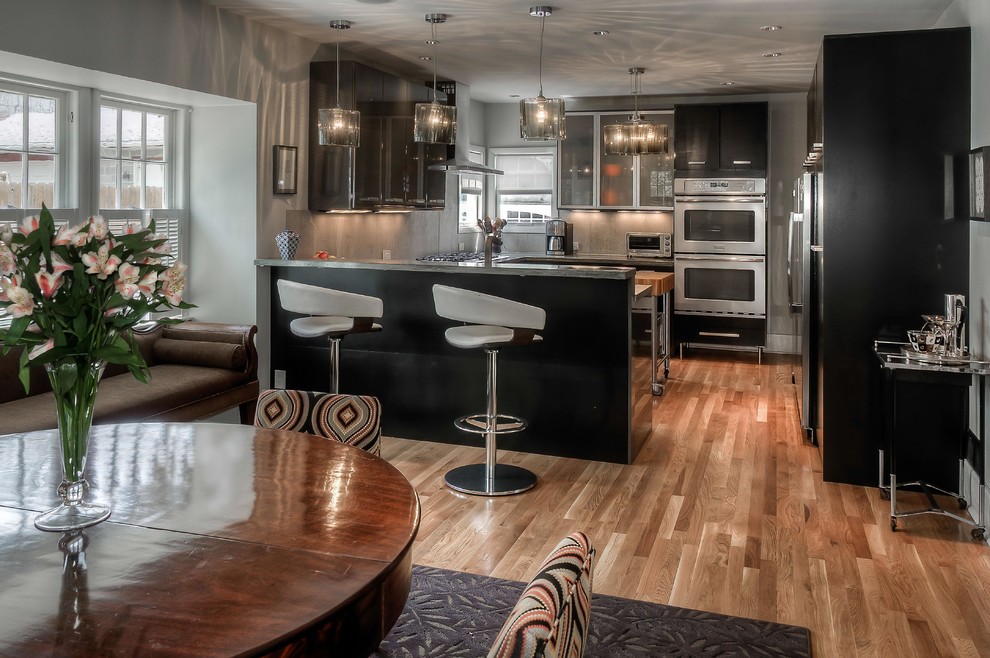 Photo of a mid-sized contemporary u-shaped eat-in kitchen in Omaha with flat-panel cabinets, black cabinets, grey splashback, medium hardwood floors, a peninsula, beige floor, concrete benchtops, ceramic splashback and stainless steel appliances.