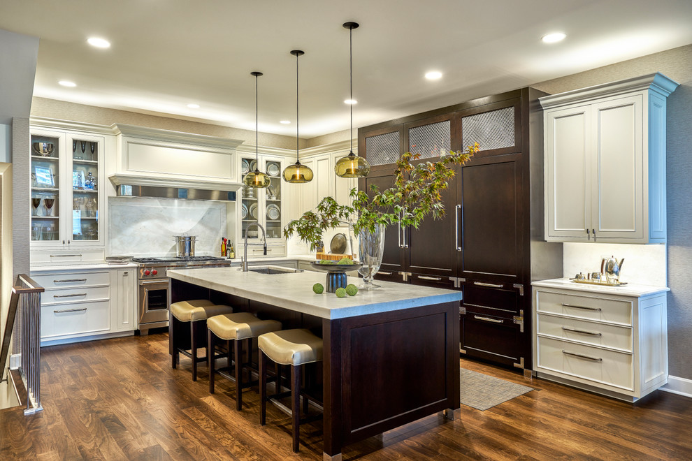 This is an example of a transitional l-shaped kitchen in Chicago with an undermount sink, recessed-panel cabinets, beige cabinets, marble benchtops, white splashback, marble splashback, panelled appliances, dark hardwood floors, with island and brown floor.