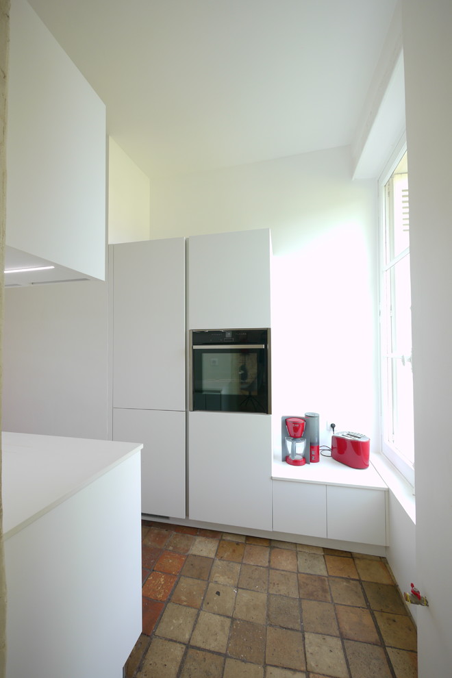 Photo of a small contemporary single-wall separate kitchen in Angers with an undermount sink, flat-panel cabinets, white cabinets, white splashback, stainless steel appliances, terra-cotta floors, no island, brown floor and white benchtop.