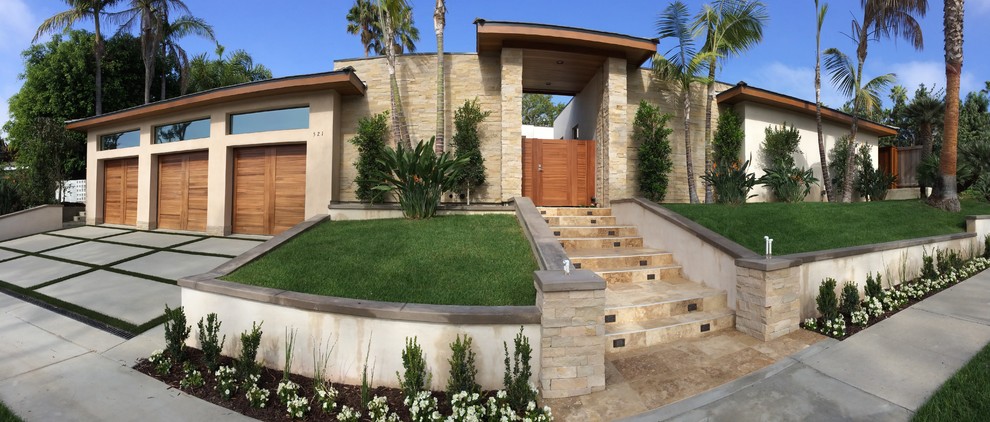 Mid-sized tropical split-level beige house exterior in Orange County with stone veneer and a flat roof.