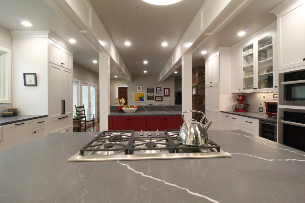 This is an example of a mid-sized country galley open plan kitchen in Seattle with a farmhouse sink, shaker cabinets, red cabinets, quartz benchtops, grey splashback, cement tile splashback, panelled appliances, medium hardwood floors, multiple islands, brown floor, grey benchtop and exposed beam.