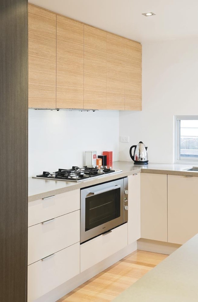 Inspiration for a small contemporary l-shaped open plan kitchen in Melbourne with an undermount sink, flat-panel cabinets, white cabinets, quartz benchtops, white splashback, glass sheet splashback, stainless steel appliances, light hardwood floors and with island.