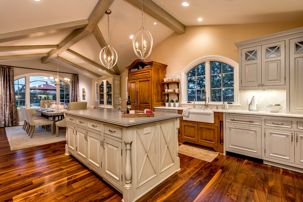 This is an example of a large traditional l-shaped open plan kitchen in San Francisco with a farmhouse sink, beaded inset cabinets, white cabinets, quartzite benchtops, beige splashback, stone tile splashback, stainless steel appliances, dark hardwood floors and multiple islands.