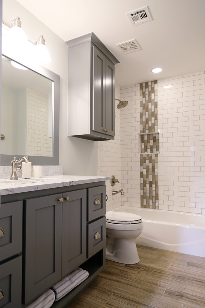 Design ideas for a mid-sized country 3/4 bathroom in Other with shaker cabinets, grey cabinets, white tile, subway tile, white walls, an undermount sink, quartzite benchtops, an alcove tub, a shower/bathtub combo, vinyl floors and a two-piece toilet.